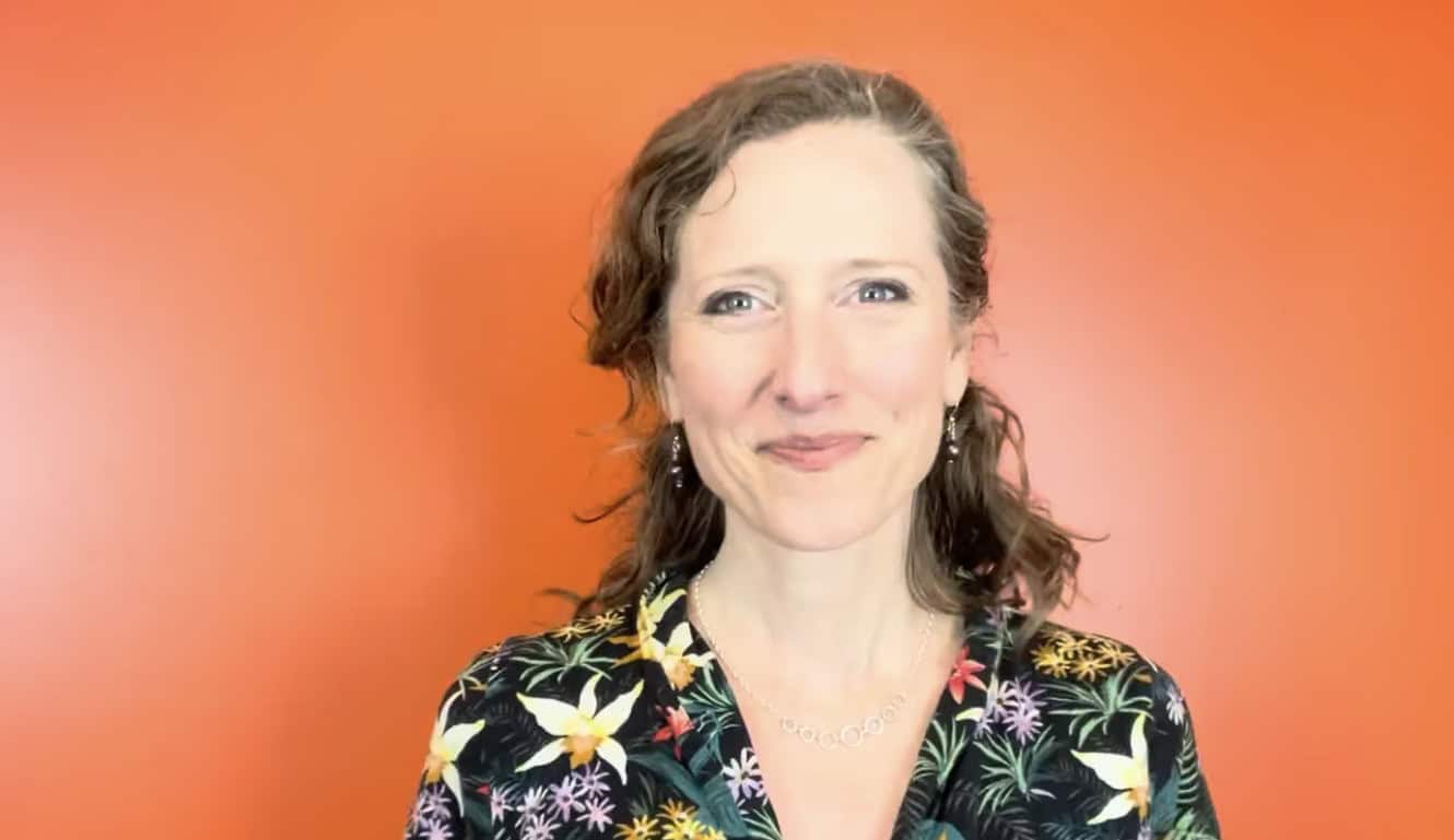 Smiling woman with floral blouse against orange background.